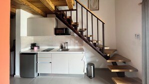 Una cocina con gabinetes blancos, un microondas, un lavamanos y una escalera con escalones de madera.