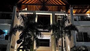 Un edificio con techo de madera triangular, paredes blancas y un balcón con barandilla de metal.