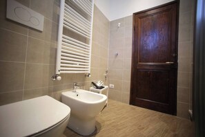 Ein Badezimmer mit Toilette, Bidet, Handtuchhalter und einer Holztür.