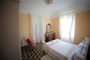 Ein Schlafzimmer mit Schachbrettfußboden, einem Bett mit weißer Bettwäsche, einem Schminktisch, einem Spiegel und einem Schaukelstuhl.