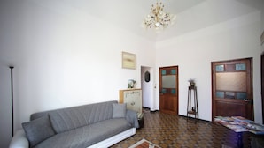 A living room with a sofa, a coffee table, a chandelier, a door with glass panels, and a patterned floor. - Au Petit Bonheur Apart (Rapallo)