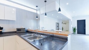 Une cuisine moderne dotée d’un îlot central, d’appareils électroménagers en acier inoxydable et de luminaires suspendus.