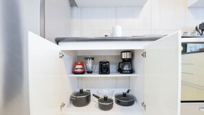 Une cuisine avec des meubles blancs, une machine à café, un mixeur et deux casseroles sur le plan de travail.