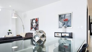Un salon moderne avec une table à manger en verre, un canapé et deux tableaux accrochés au mur.