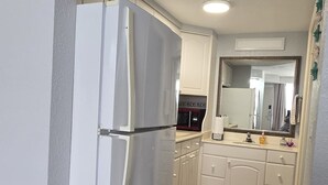 A compact kitchen with white cabinets, a white refrigerator, and a small trash bin. - Cozy studio in a fantastic Daytona Beach location (Daytona Beach)