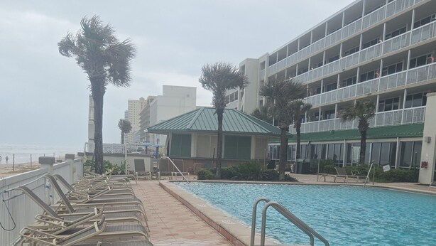 A swimming pool with lounge chairs, a building with balconies, and palm trees. - Cozy studio in a fantastic Daytona Beach location (Daytona Beach)