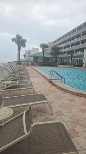 Une piscine avec des chaises longues, un bâtiment doté de balcons et des palmiers.