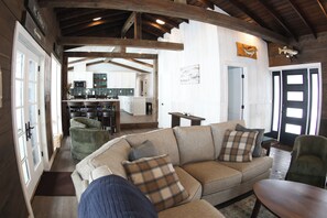 A living room with a sofa, a coffee table, and a green chair. There is a kitchen in the background with cabinets and a microwave.