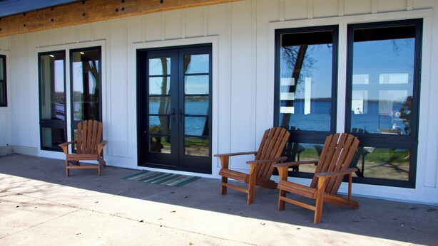 A building with large windows, a wooden deck, and two wooden chairs. - Modern Lakeside Retreat: Ultimate Group Getaway (Dent)