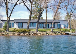 A modern house by a lake with a dock, large windows, and a well-maintained lawn.