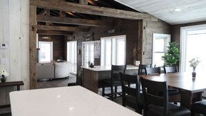 Une salle à manger spacieuse avec un plafond haut et des poutres apparentes, une grande table blanche et plusieurs chaises sombres.