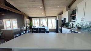 A modern kitchen with a large island, wooden ceiling beams, and a view of the outdoors. - Modern Lakeside Retreat: Ultimate Group Getaway (Dent)