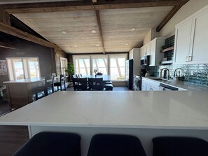 A modern kitchen with a large island, wooden ceiling beams, and a view of the outdoors. - Modern Lakeside Retreat: Ultimate Group Getaway (Dent)