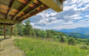 A covered outdoor area with a wooden ladder, surrounded by lush greenery and a mountainous landscape.