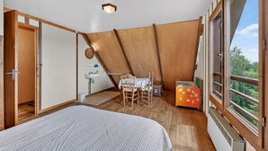 Een slaapkamer met een bed, een klein tafeltje met een stoel, een raam en uitzicht op groen buiten.