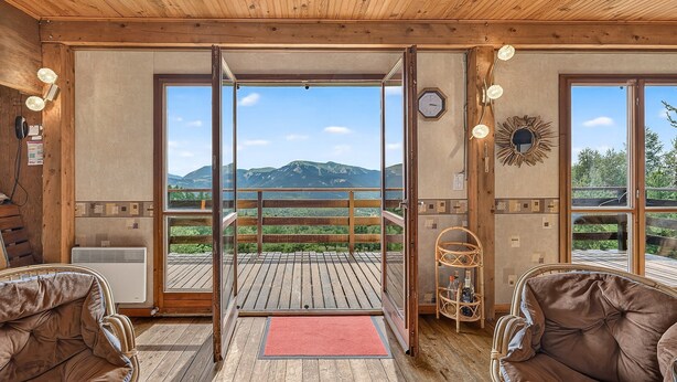 A wooden interior with a balcony, two brown leather sofas, a wicker side table, and a red doormat. - Chalet with Mountain Views, Private Garden and Balcony (Seyne)
