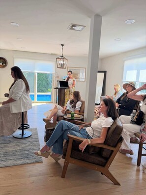 A spacious living room with a high ceiling, a central chandelier, and a view of the outdoors through large windows.