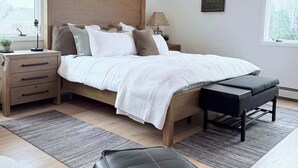 A modern bedroom with a wooden bed, bedside tables, a bench, and a wall-mounted sign. - 2 minute free ride to Shinnecock Golf US Open (Southampton)