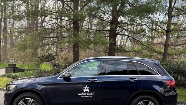 A dark-colored SUV parked on a paved surface with a wooded area in the background. - 2 minute free ride to Shinnecock Golf US Open (Southampton)