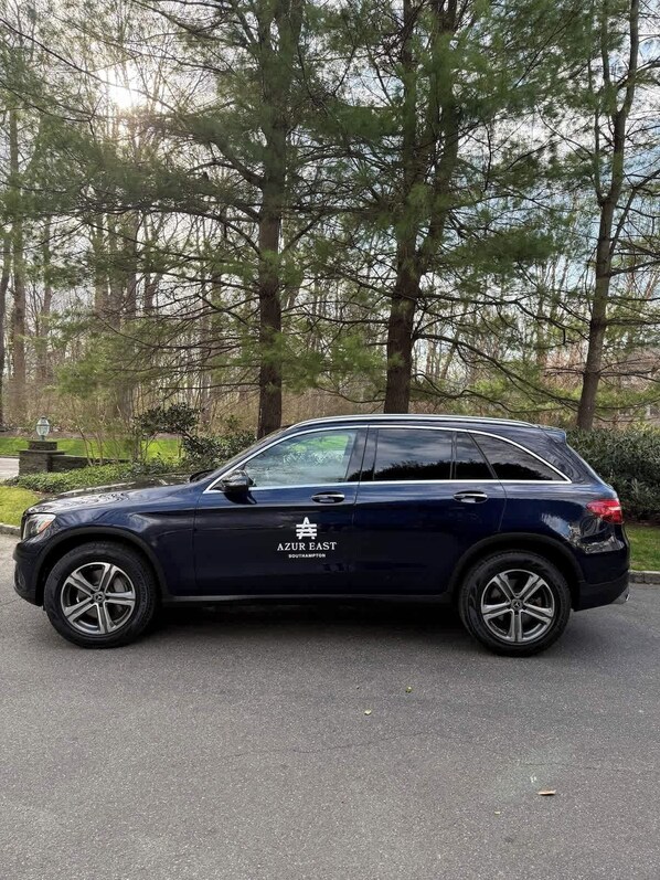 A dark-colored SUV parked on a paved surface with a wooded area in the background.
