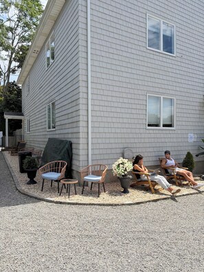 A building with a grey siding exterior, a covered patio area with wicker chairs, and a small potted plant.