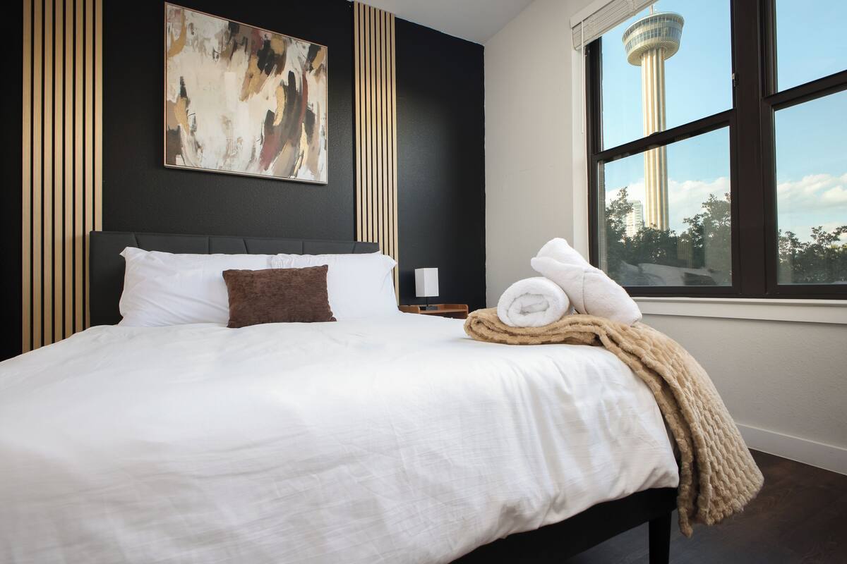 A hotel room with a large bed, a view of a tower, and a painting on the wall.