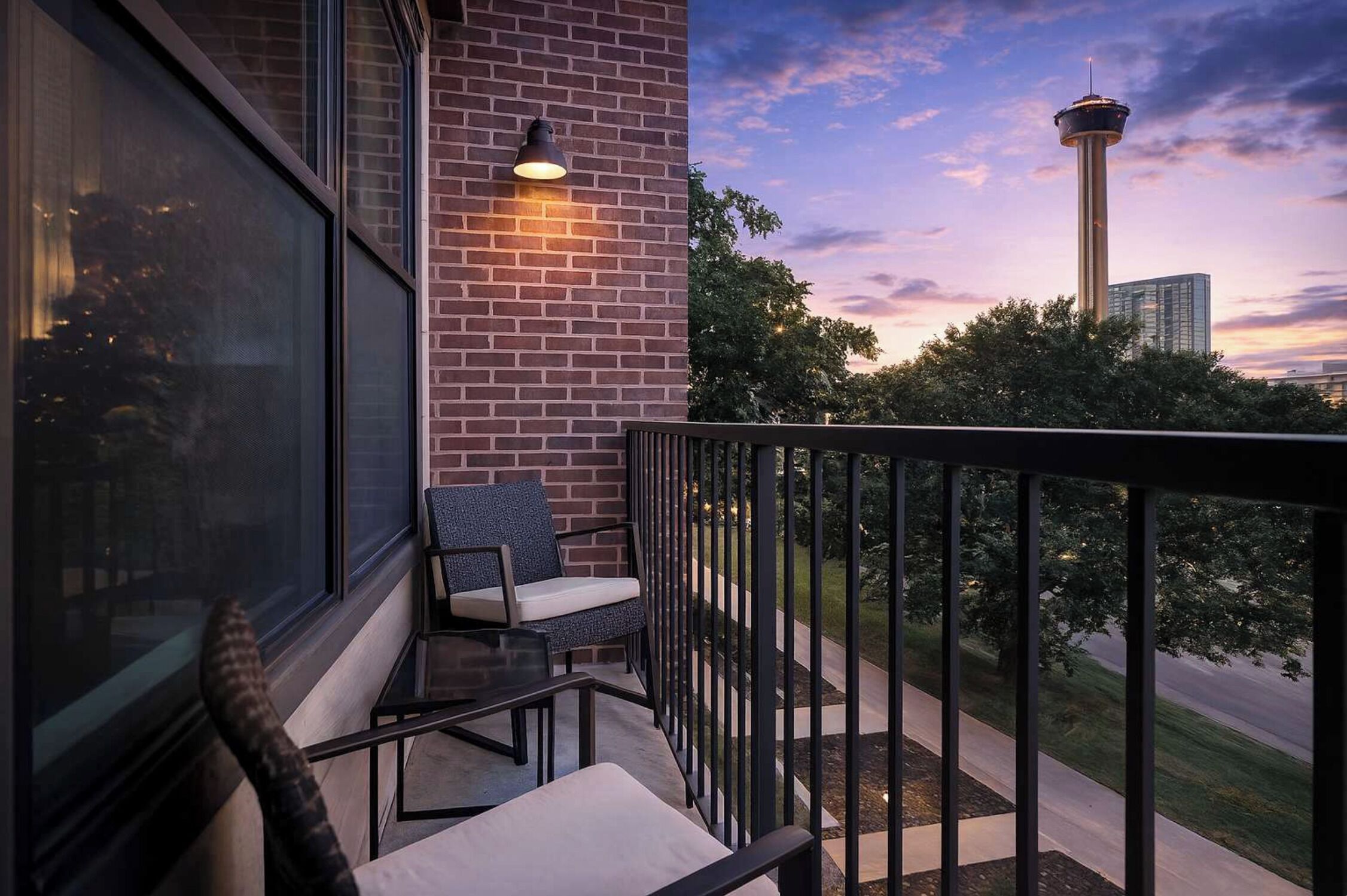 A balcony with a chair, a table, and a view of a tower and trees.
