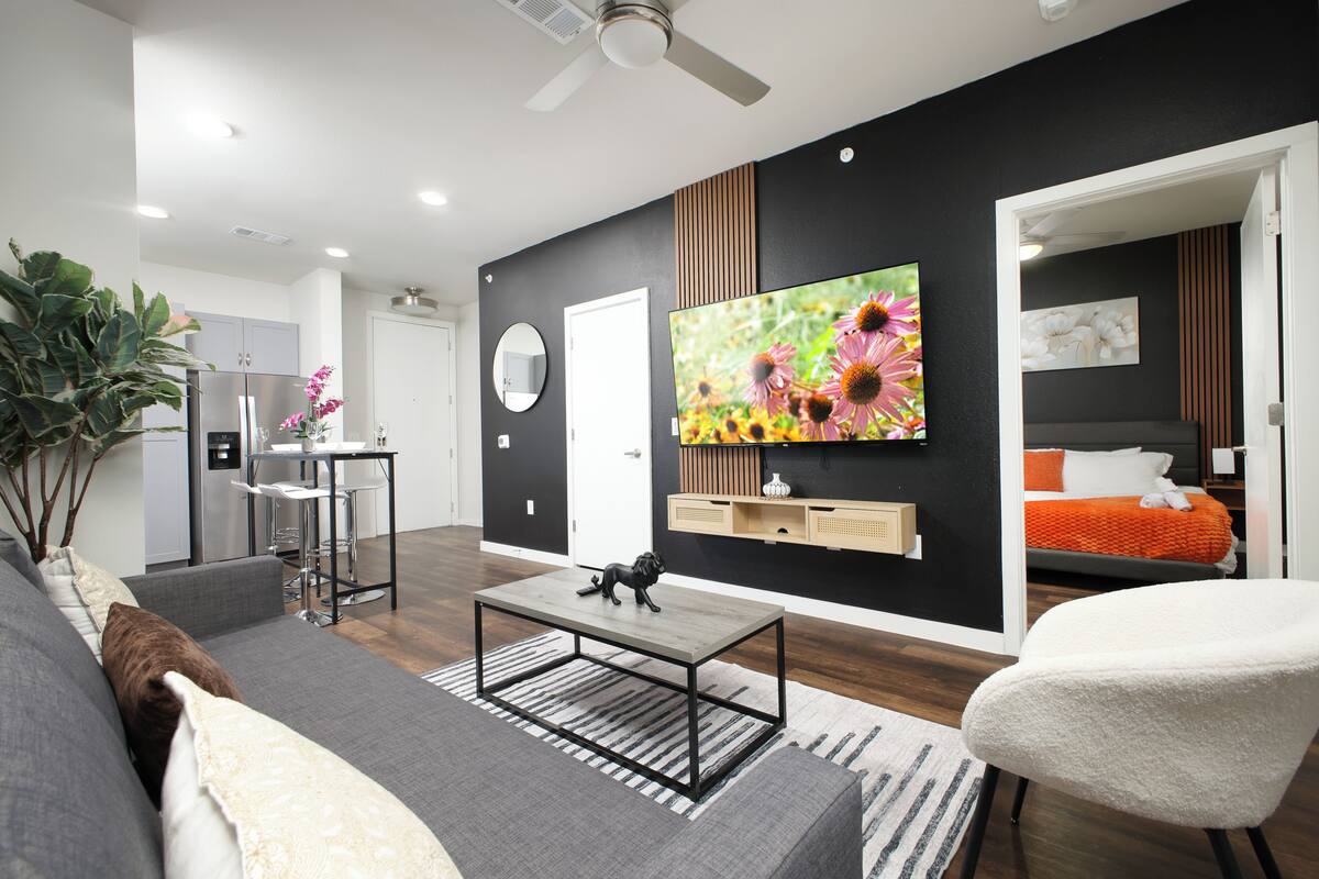 A modern living room with a sofa, a coffee table, a TV, and a dining area with chairs.