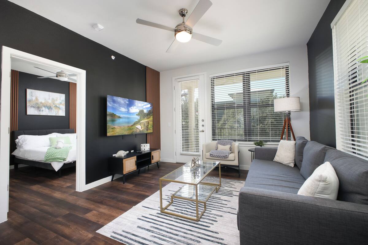 A modern living room with a bed, sofa, TV, and a ceiling fan.