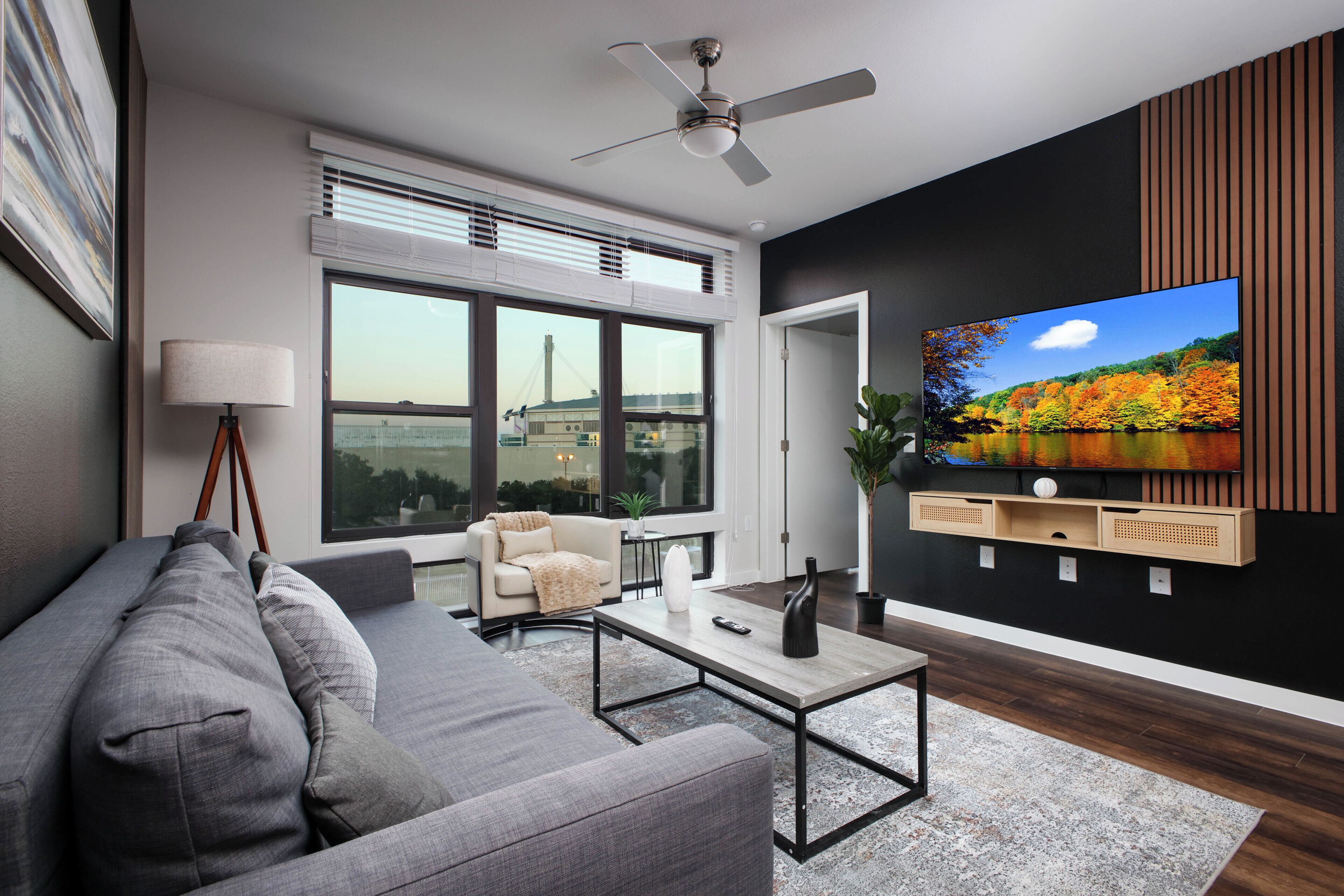 A modern living room with a sofa, coffee table, TV, and large windows.