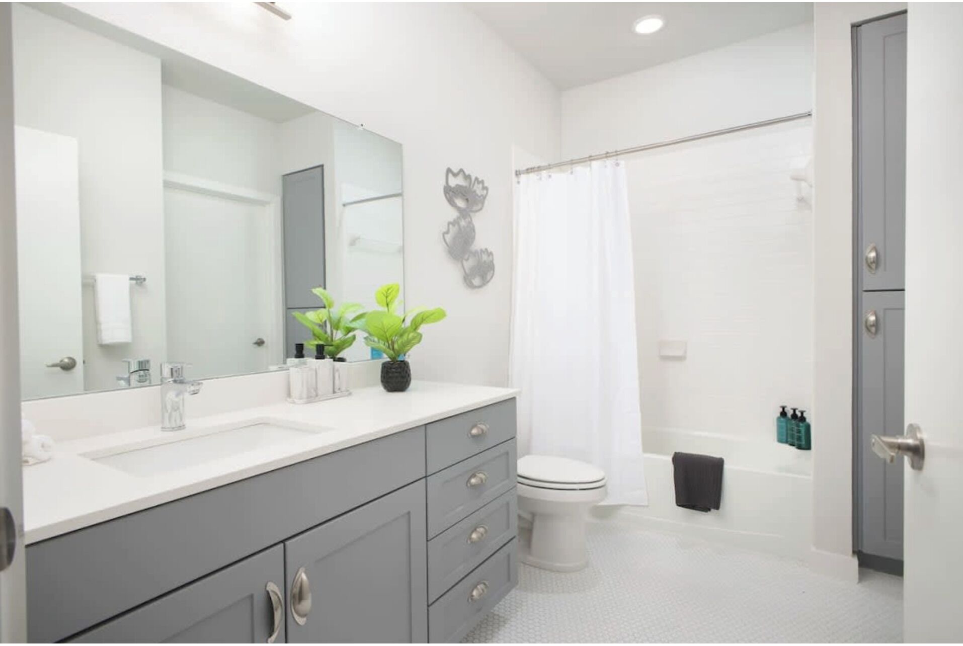 A modern bathroom with a large mirror, grey cabinets, a white sink, a toilet, and a shower curtain.