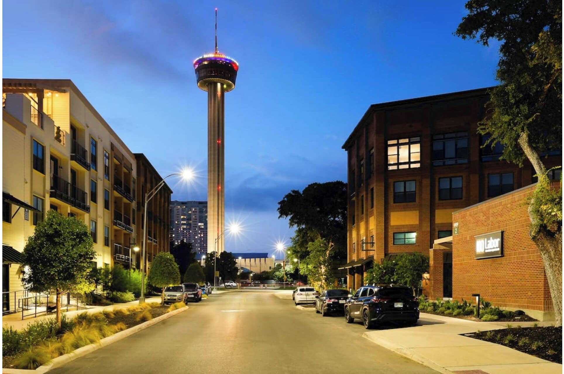 A street view with a tower in the background, surrounded by multi-story buildings with balconies.