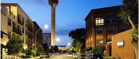 A street view with a tower in the background, surrounded by multi-story buildings with balconies.