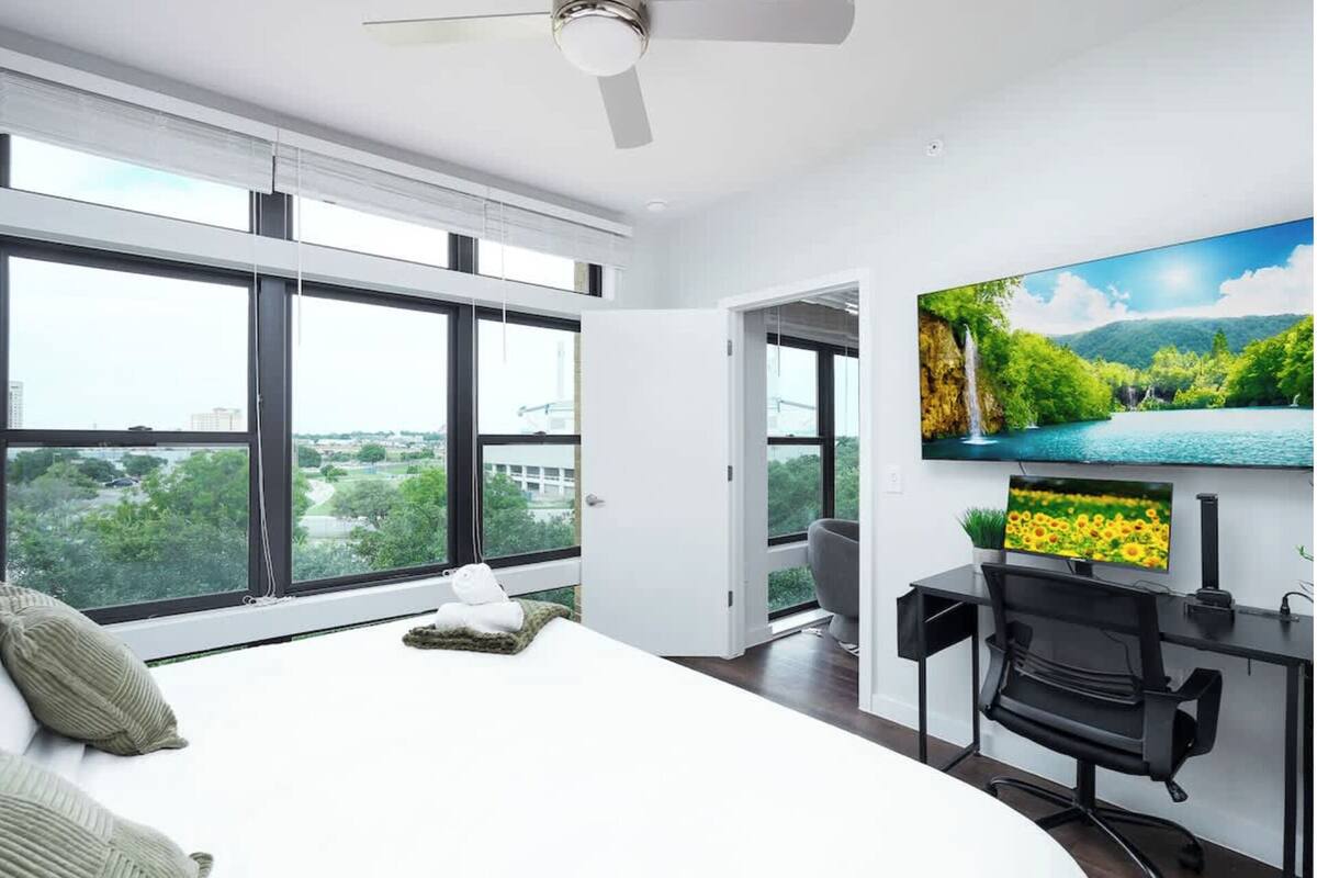 A modern bedroom with a large bed, a desk, and a TV displaying a nature scene.