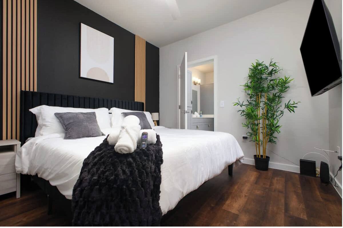 A hotel room with a bed, a TV, a plant, and a bathroom visible through an open door.