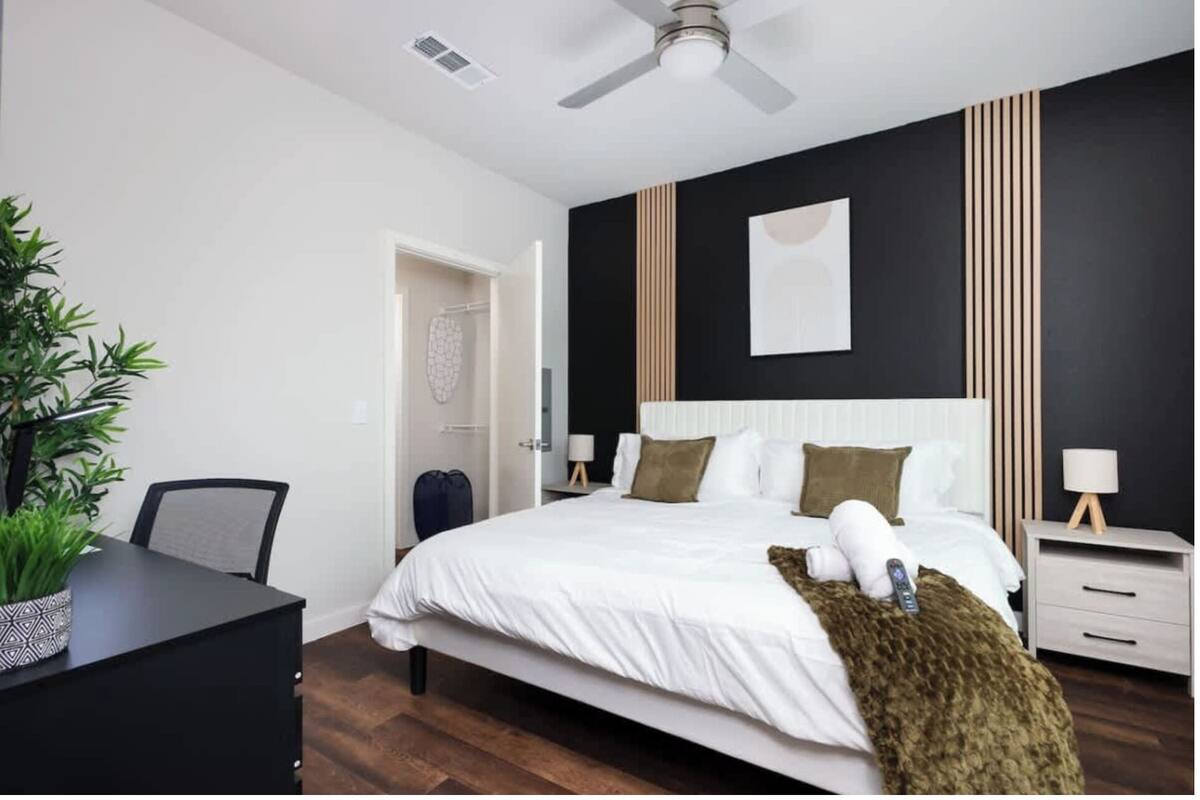 A modern bedroom with a bed, bedside tables, a desk, and a ceiling fan.