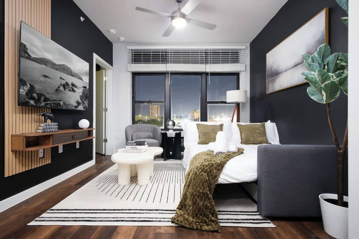 A modern bedroom with a bed, a desk, a chair, a sofa, and a large window.