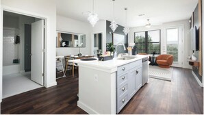 A modern kitchen with a central island, a dining area with chairs, a large mirror, and a view through the glass door. - Labor by Stylish Stays (San Antonio)