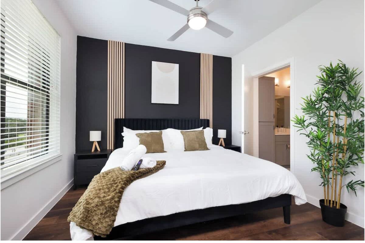 A modern bedroom with a bed, bedside tables, a ceiling fan, and a potted plant.