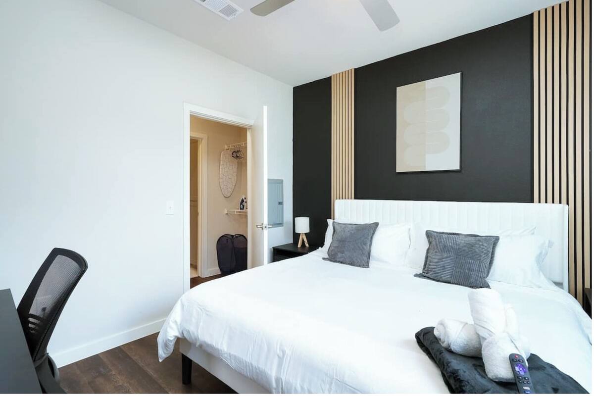 A modern hotel room with a large bed, a desk, a chair, and a bathroom visible through an open door.