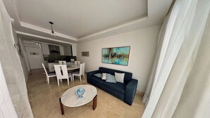 Uma sala de estar com um sofá azul, uma mesa de centro redonda e um quadro na parede.