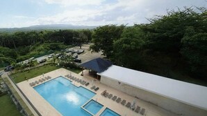 Piscina com espreguiçadeiras e área coberta, cercada por vegetação e vista distante de colinas.