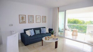 Uma sala de estar moderna com um sofá azul escuro, uma mesa de centro redonda e uma grande porta de vidro deslizante que dá para uma varanda externa.