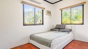 A bedroom with a bed, two windows, and an air conditioning unit. - 3-bedroom estate in serene Calatagan with cool AC breeze (Calatagan)
