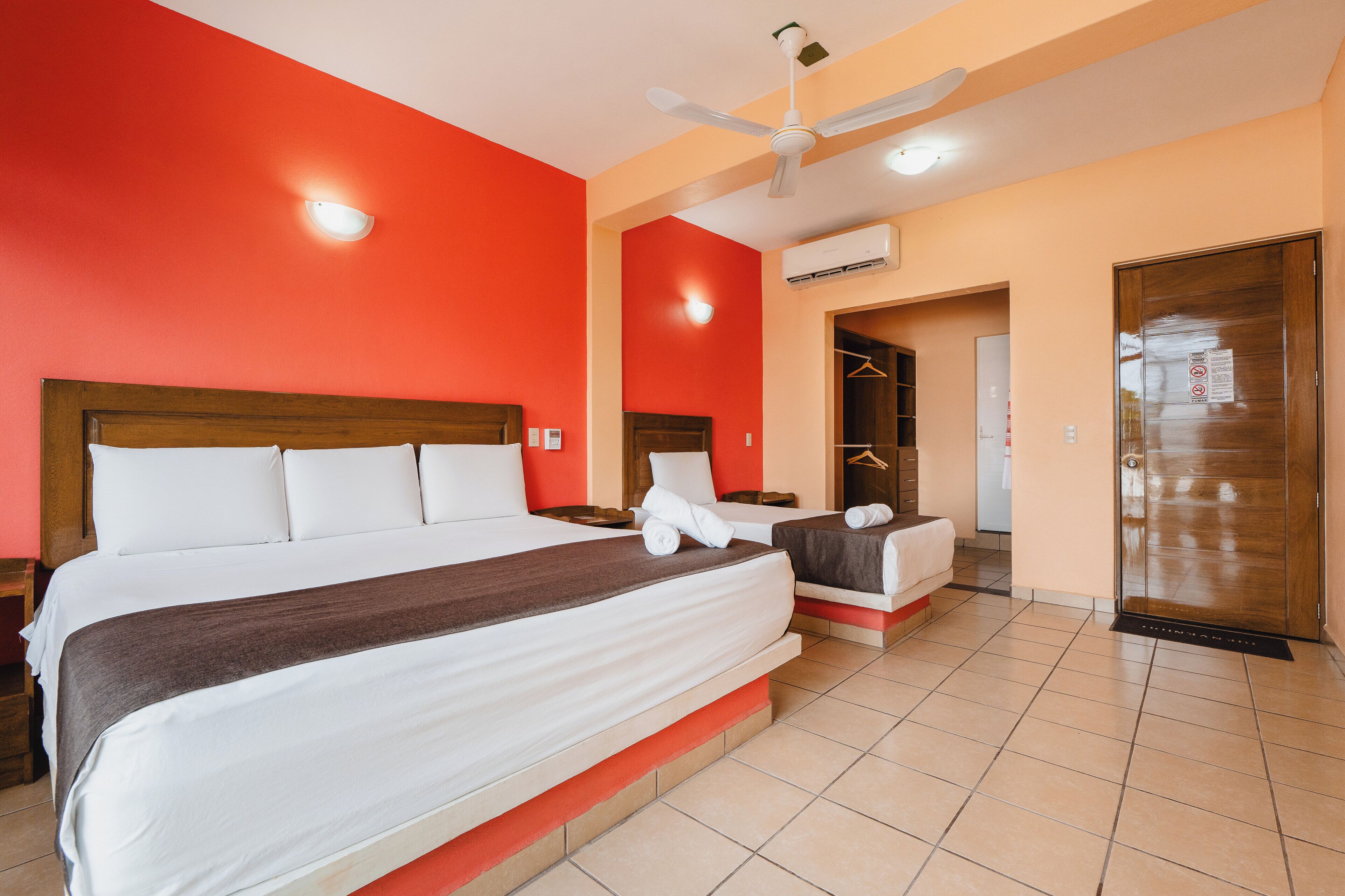 A hotel room with a large bed, a ceiling fan, an air conditioning unit, and a wardrobe.