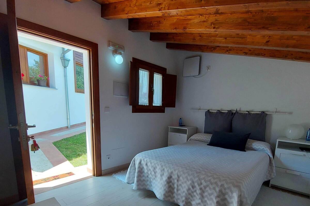 A bedroom with a bed, bedside tables, a nightstand, a window with curtains, and a wooden ceiling.