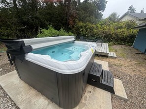 Een hottub met een houten terras, omgeven door bomen en een tuinhuis.