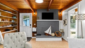 A cozy living room with a fireplace, wooden shelves, and a television. - Coastal Woodlands A-Frame Sanctuary with Hot Tub (Heceta Beach)