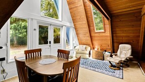 A cozy room with a wooden ceiling, a dining table with chairs, a sofa, and a chair. - Coastal Woodlands A-Frame Sanctuary with Hot Tub (Heceta Beach)