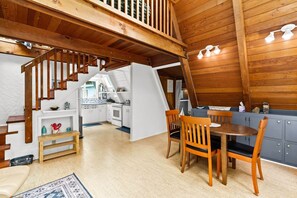 Un espace de vie de style loft avec un escalier en bois, un coin repas avec des chaises en bois et une cuisine visible à travers une porte ouverte.